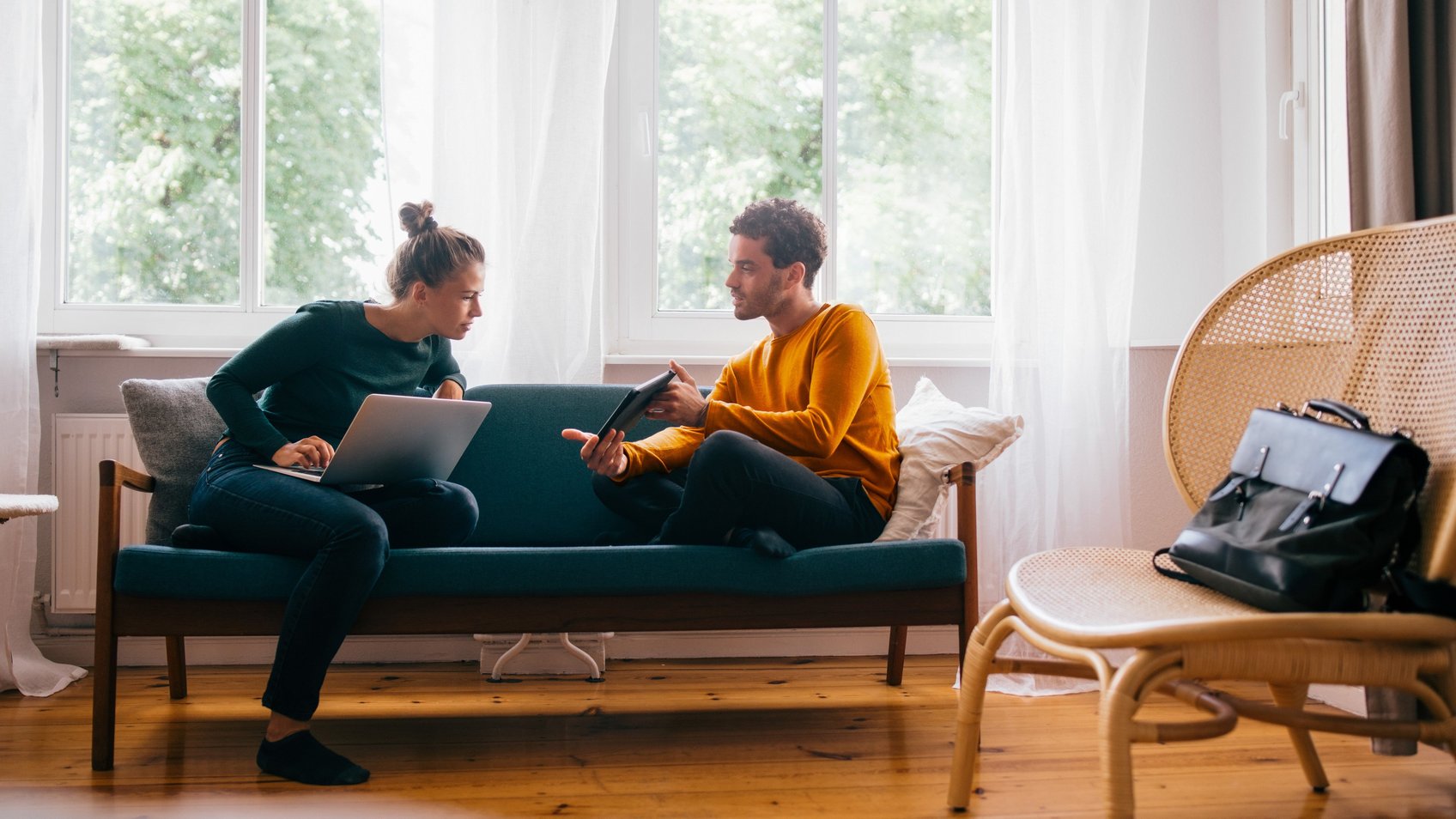 Kvinde og mand sidder i sofa og kigger på computer og tablet 